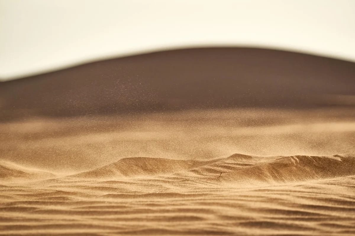 Primer plano de una duna en el desierto, con arena fina desplazándose por el viento