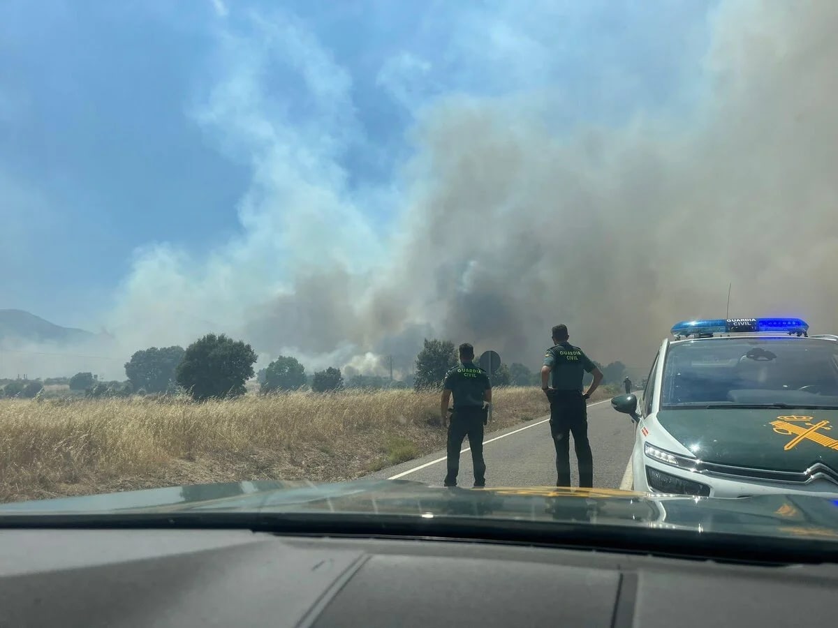 Agentes de la Guardia Civil vigilan el avance de un incendio forestal en Navaluenga, Ávila, con humo denso y vehículo oficial en primer plano