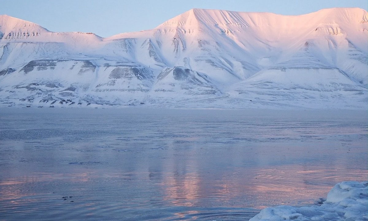 Montañas cubiertas de nieve en Svalbard con luz rosada de atardecer sobre el hielo