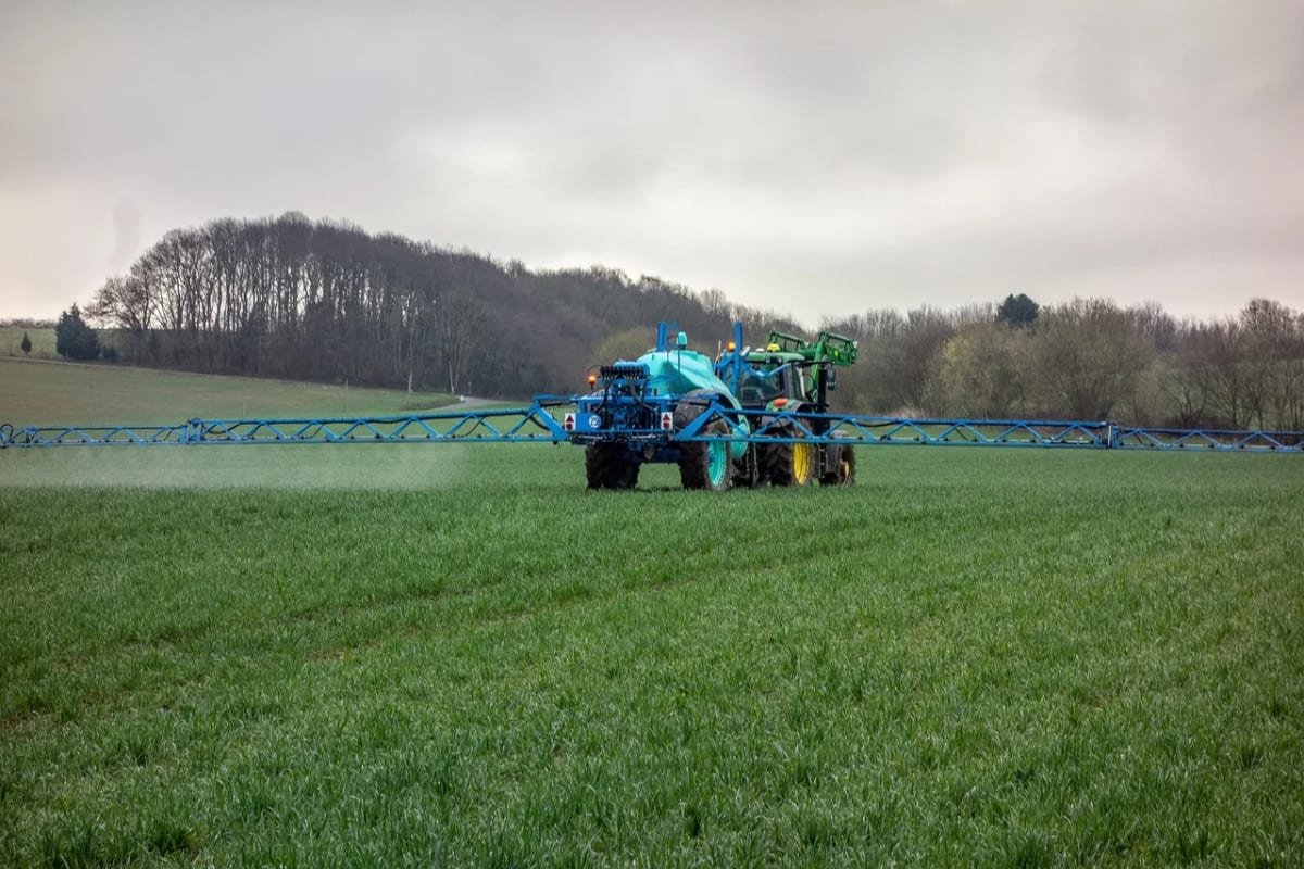 Tractor agrícola aplicando fertilizante líquido en un campo verde, con árboles al fondo y cielo nublado