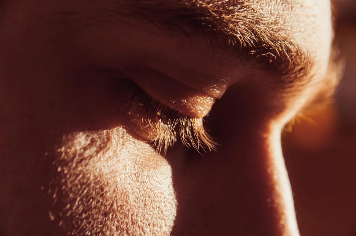 Primer plano de un ojo humano cerrado bajo luz cálida, mostrando detalles de las pestañas y la textura de la piel