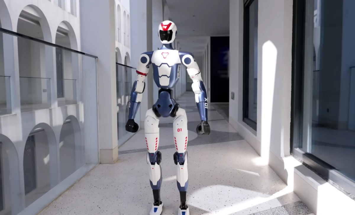 Robot humanoide Unitree R1 posando en un pasillo moderno iluminado por la luz natural, mostrando su diseño compacto y avanzado