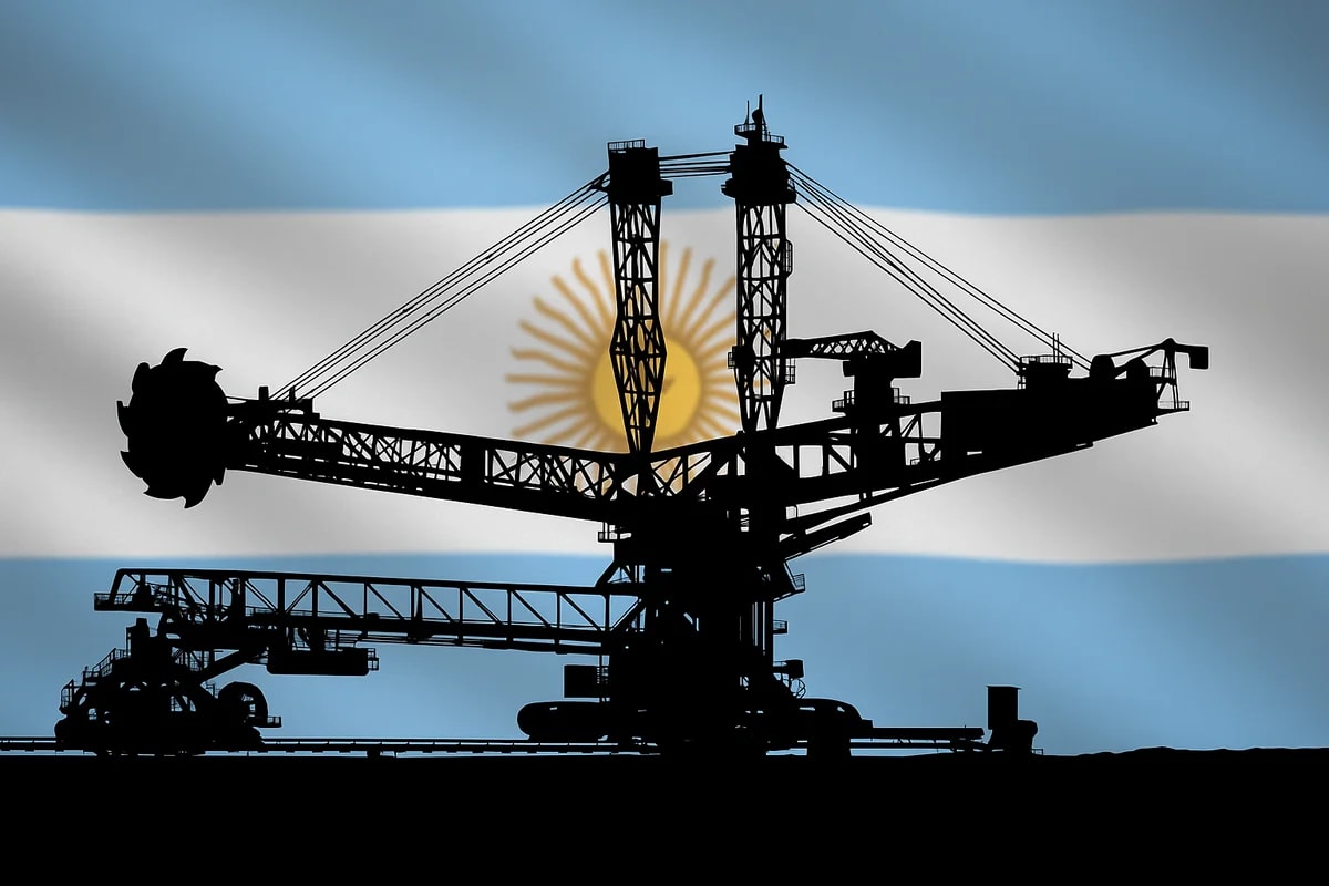 Silueta negra de una excavadora de rueda de cangilones frente a una bandera argentina