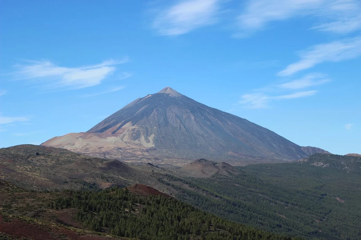 Vista panorámica del volcán Teide en Tenerife, con cielos despejados y laderas cubiertas de vegetación