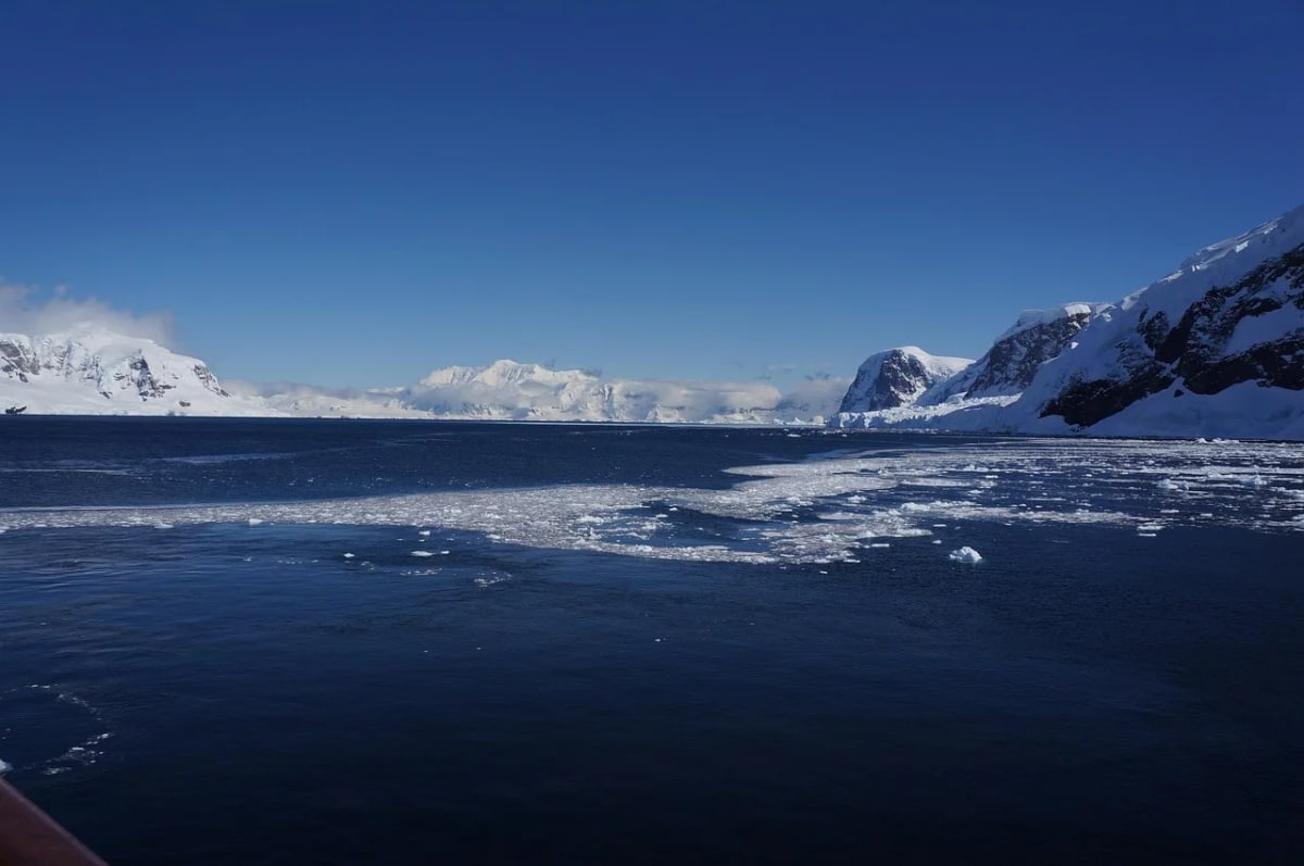 Paisaje antártico con montañas nevadas, hielo flotante y aguas profundas bajo un cielo despejado