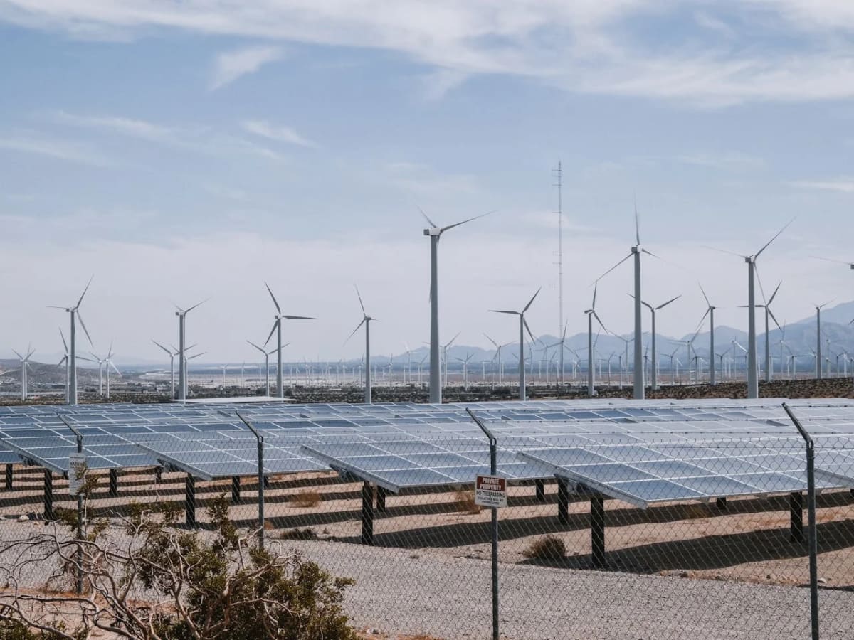 Plantas solares y parque eólico en un paisaje desértico con montañas al fondo