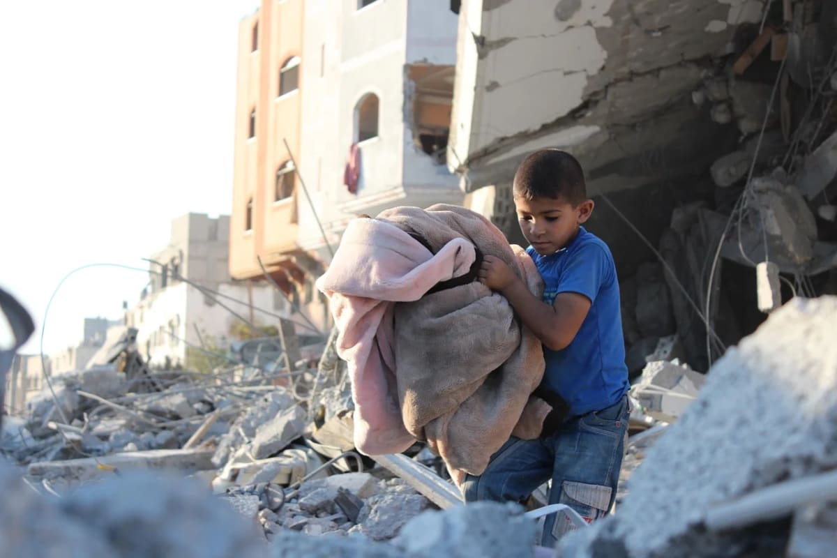 Niño en Gaza camina entre escombros tras un bombardeo sosteniendo mantas en sus brazos