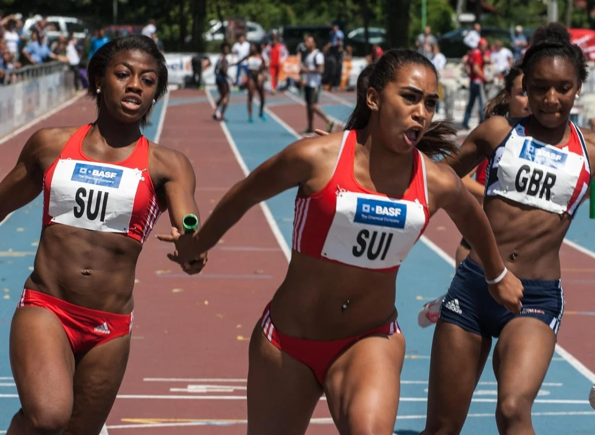 Atletas compiten en una carrera de relevos femeninos en pista de atletismo durante el momento del pase del testigo