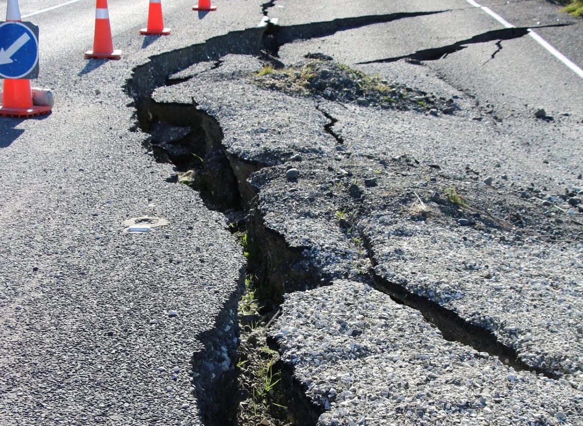 Carretera dañada y agrietada tras un terremoto, con conos de seguridad delimitando la zona afectada