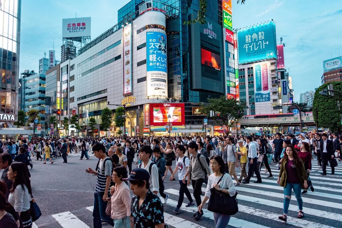 Multitud de personas cruzando un paso peatonal en una ciudad de Tokio, rodeada de edificios iluminados y anuncios publicitarios