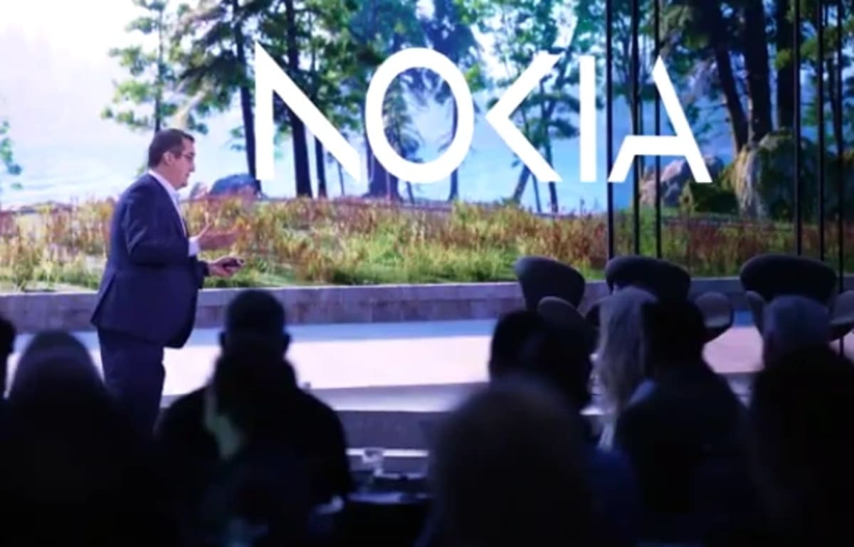 Ejecutivo de Nokia en el escenario durante una conferencia, con el logotipo de la compañía proyectado en grande sobre un fondo natural de árboles