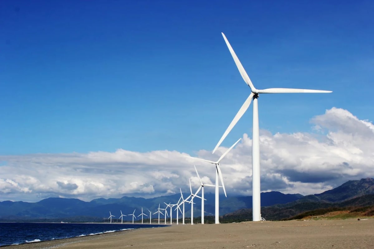 Fila de aerogeneradores en la costa con montañas al fondo y cielo azul