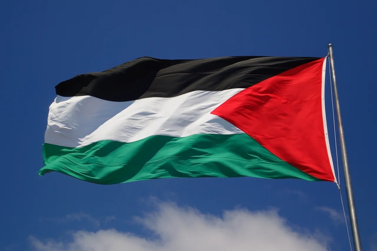 Bandera de Palestina ondeando contra un cielo azul despejado con algunas nubes