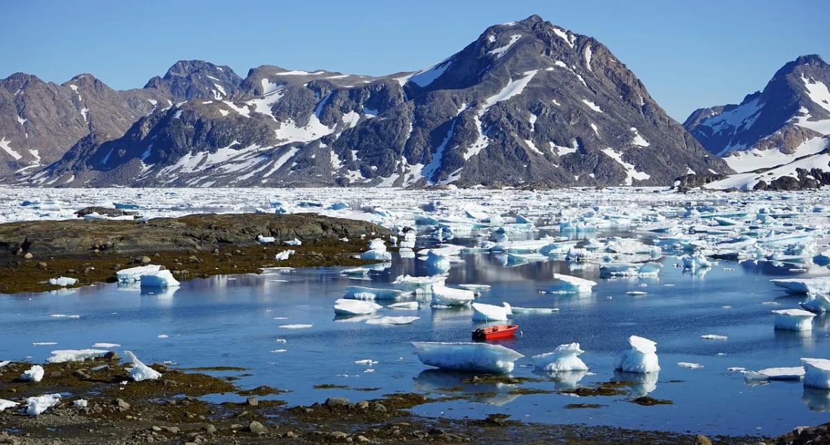 Paisaje de Groenlandia con montañas nevadas, bloques de hielo flotando y agua cristalina en primer plano