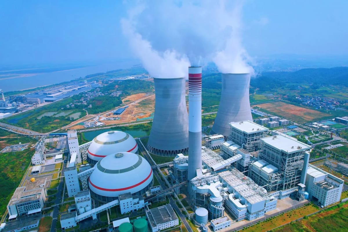 Vista aérea de una central termoeléctrica con torres de refrigeración y chimenea emitiendo vapor