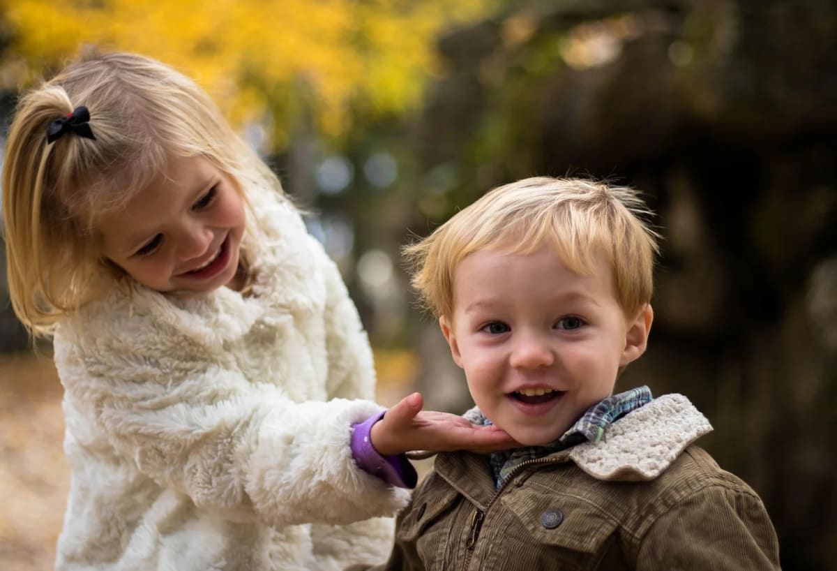 Dos niños rubios pequeños jugando al aire libre en un entorno natural con hojas otoñales
