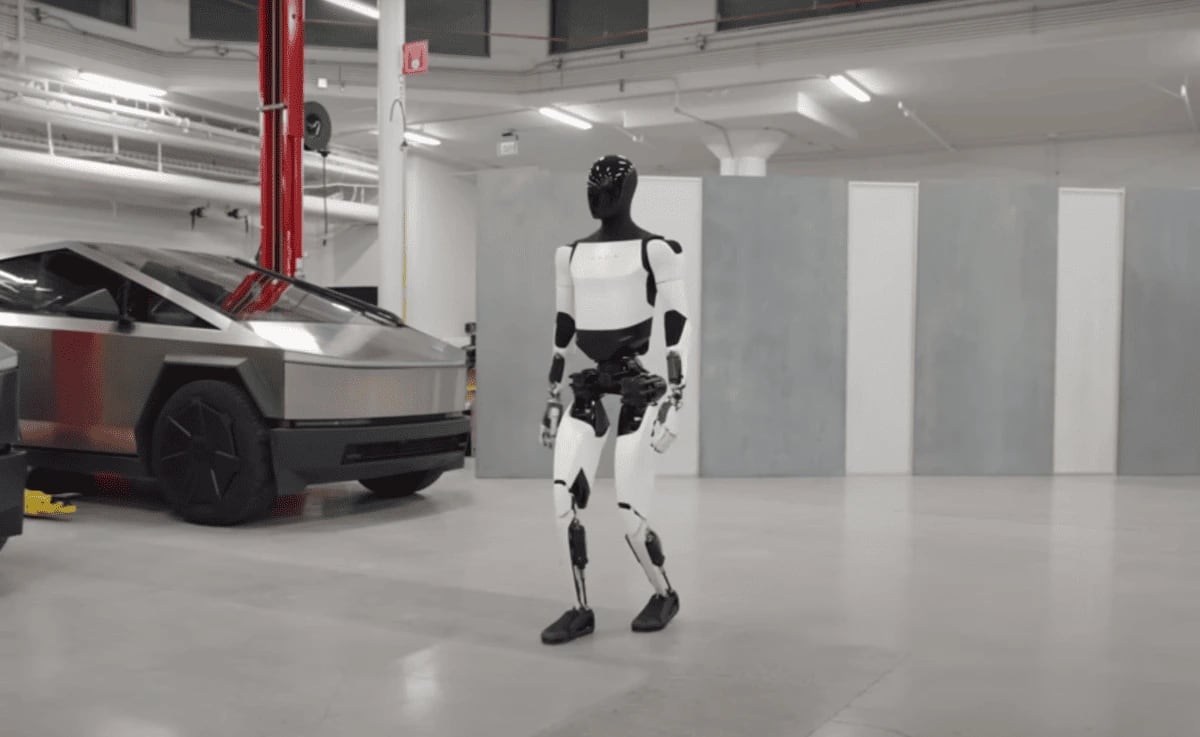 Robot humanoide Optimus de Tesla caminando en una fábrica junto a un vehículo Cybertruck
