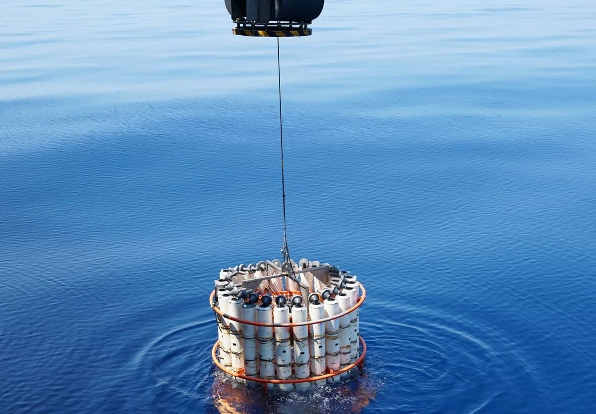 Dispositivo oceanográfico con múltiples botellas de muestreo desciende desde una grúa hacia las aguas profundas, en una operación científica en mar abierto