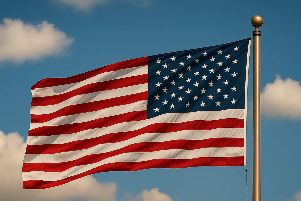 Bandera de Estados Unidos ondeando al viento sobre un asta metálica, con el cielo azul y nubes suaves de fondo