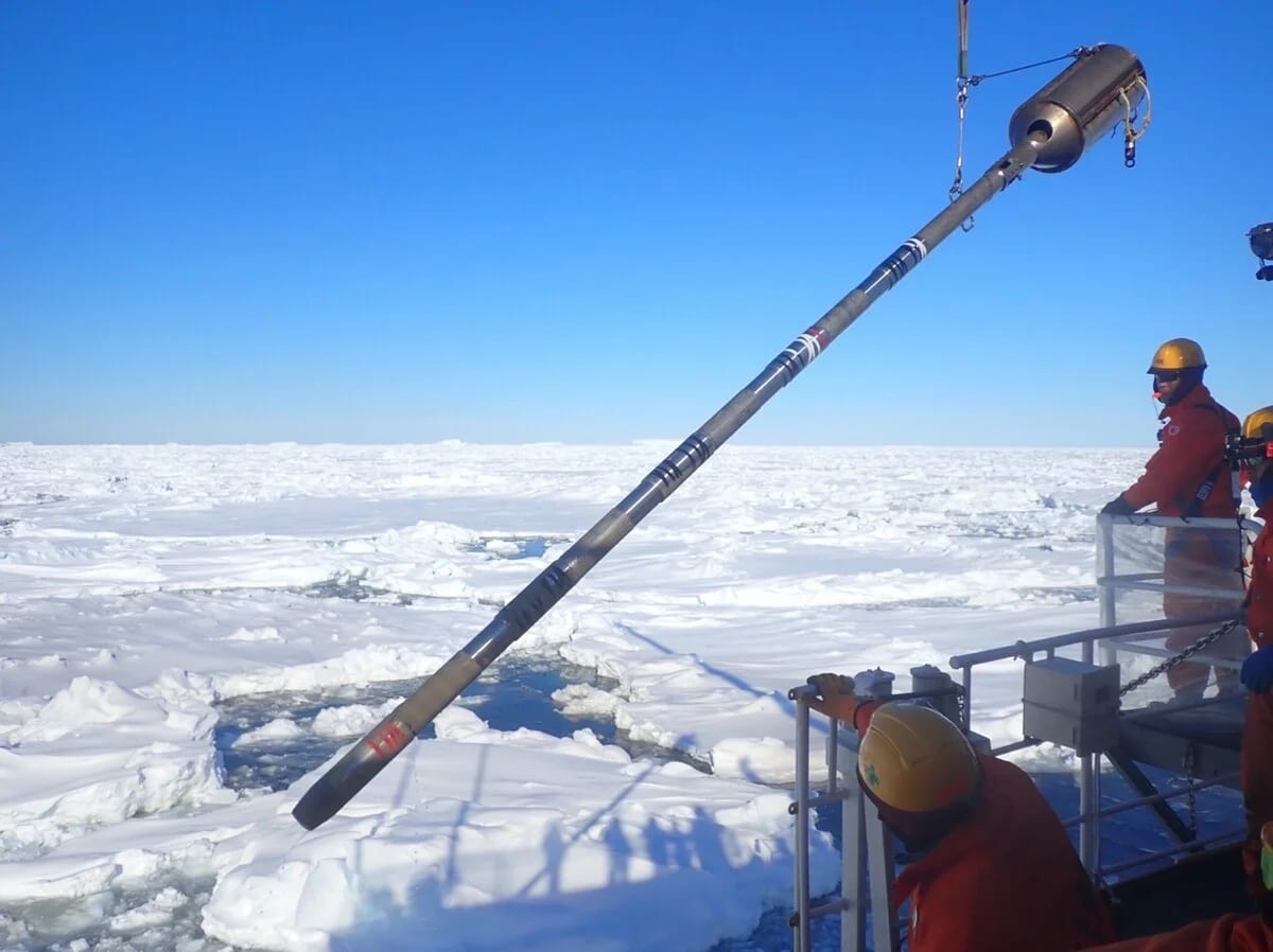 Dispositivo cilíndrico descendiendo desde una plataforma sobre el hielo marino antártico para la extracción de núcleos de sedimento