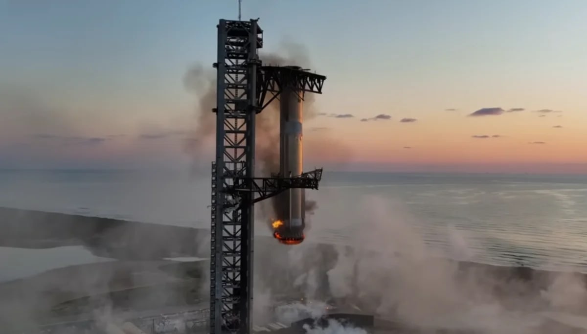 El propulsor Super Heavy desciende sobre la torre de lanzamiento entre humo y llamas durante una maniobra de captura