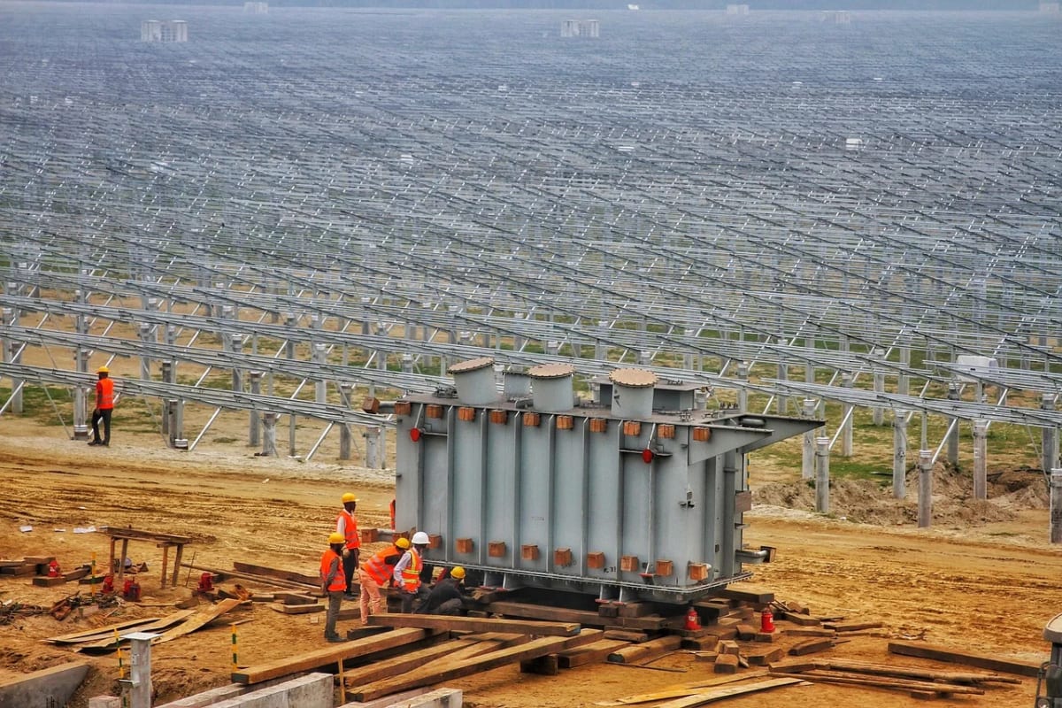 Trabajadores con cascos y chalecos de seguridad instalan un gran transformador en una planta solar