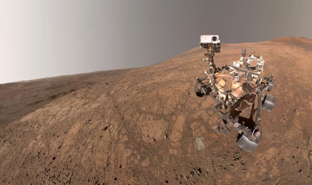 Selfi del rover Perseverance en el cráter Jezero con un pequeño remolino de polvo visible en la distancia