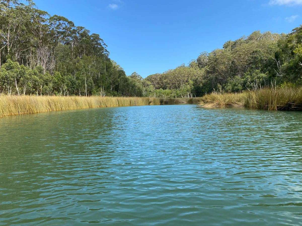 Lago de K'gari con aguas claras y nivel reducido, conectado a un sistema subterráneo más profundo