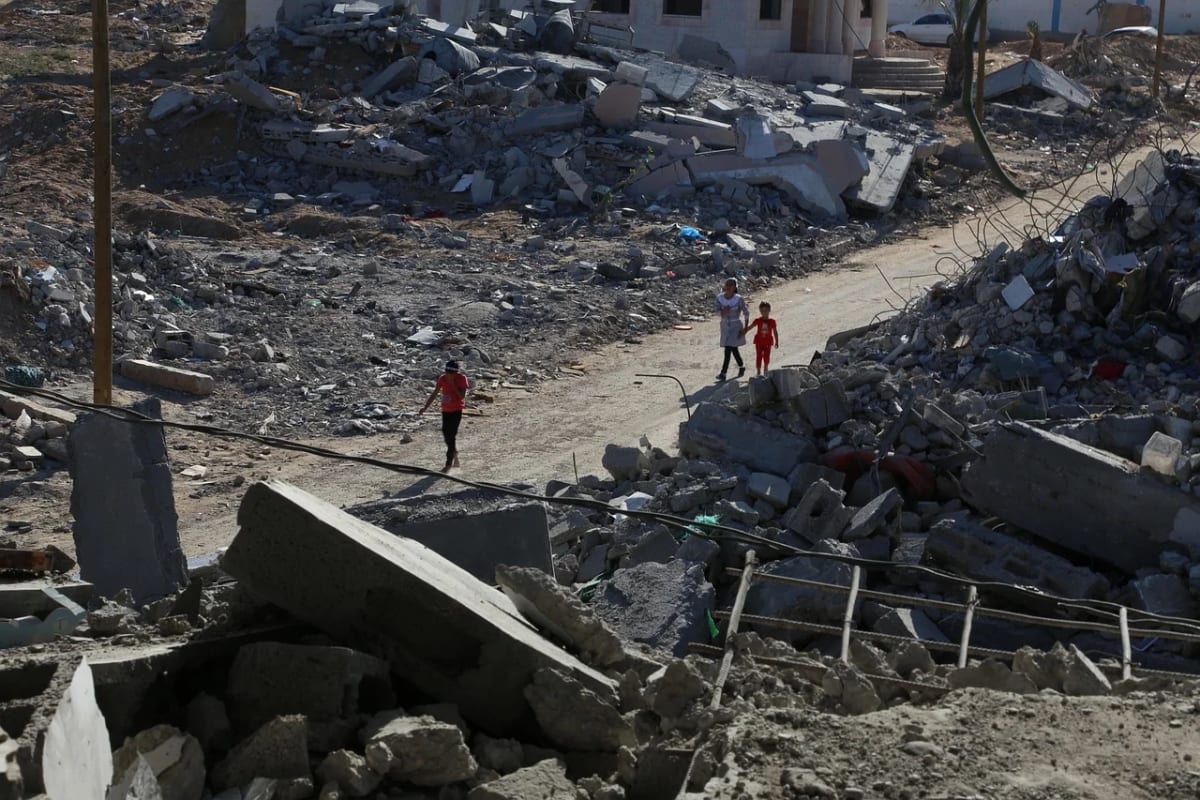 Personas caminando entre edificios destruidos en una zona devastada de Gaza