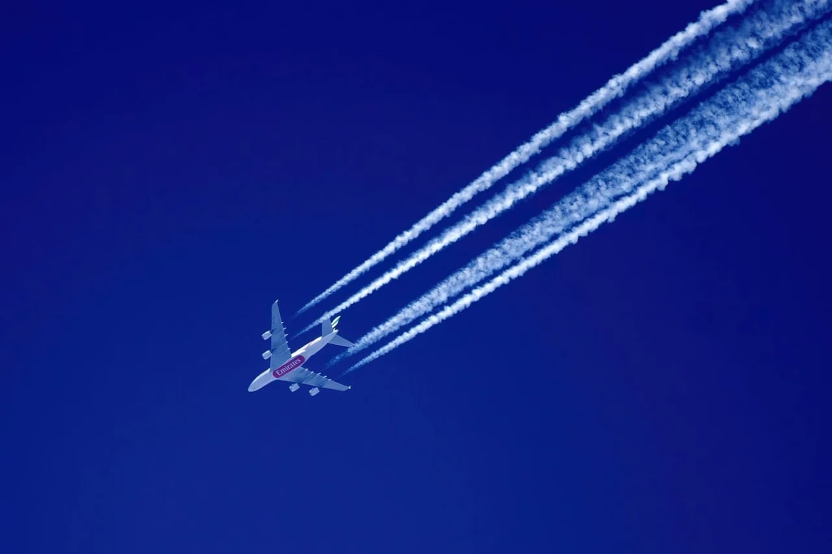 Avión comercial dejando estelas de condensación mientras vuela en un cielo azul despejado