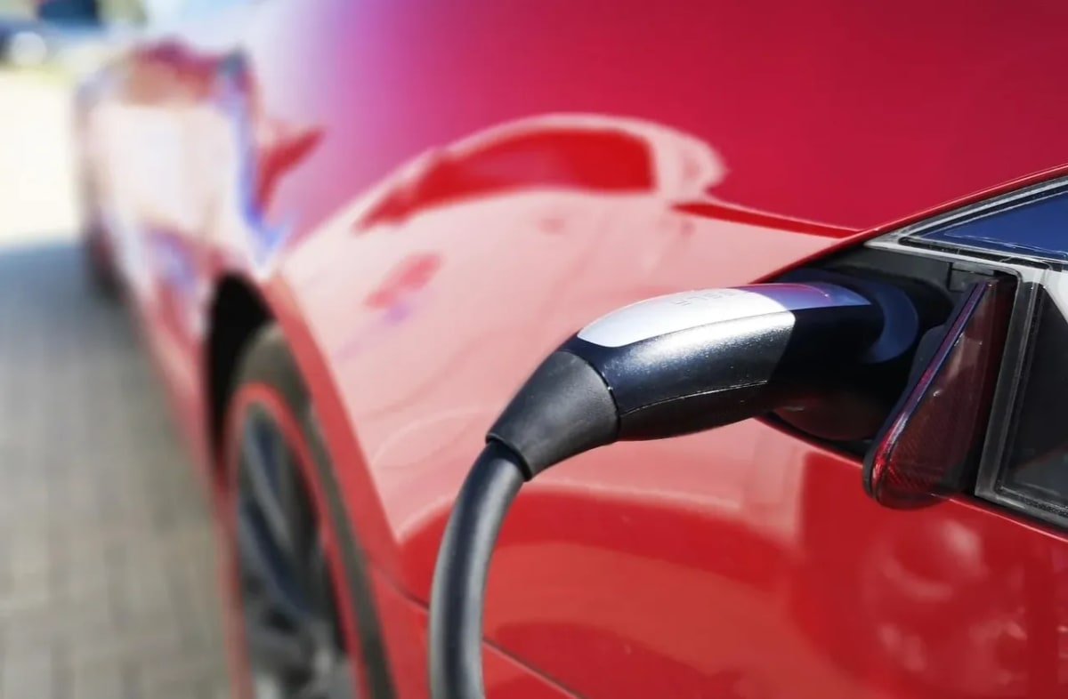 Coche eléctrico rojo conectado a un punto de carga mediante un cable