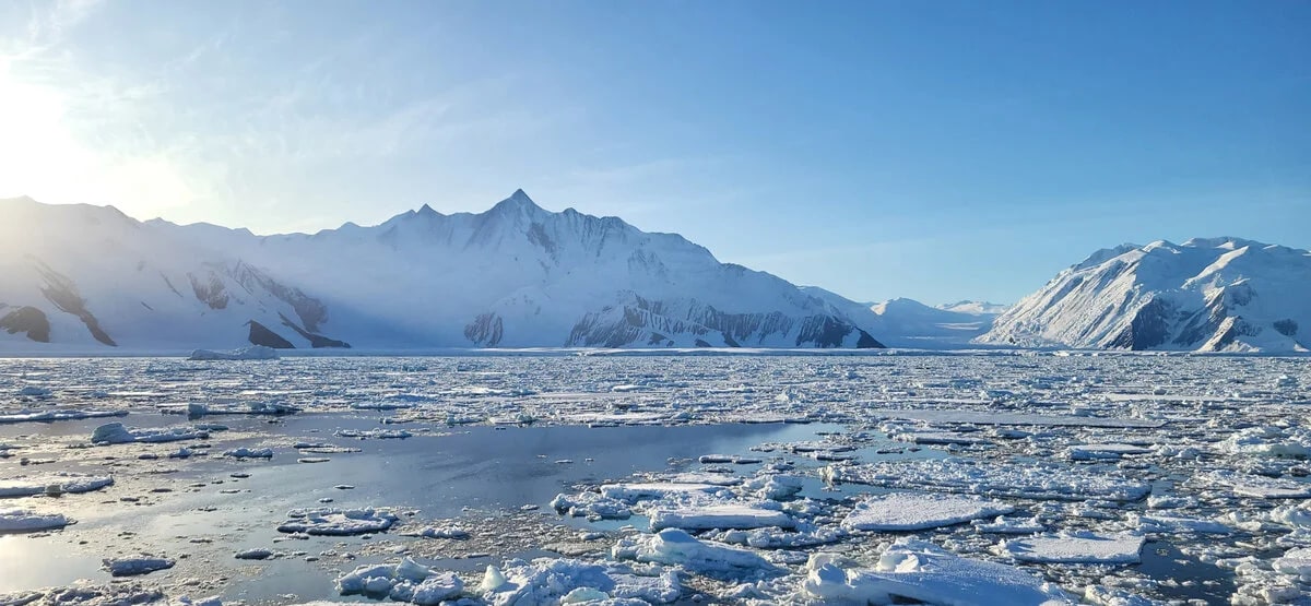 Hielo costero adherido a la costa con montañas y glaciares al fondo en la Antártida