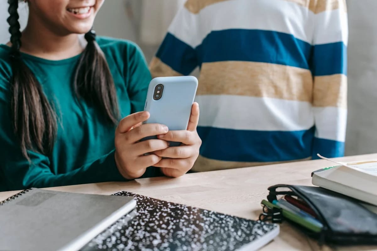 Estudiante usando un teléfono móvil sobre una mesa con cuadernos y material escolar