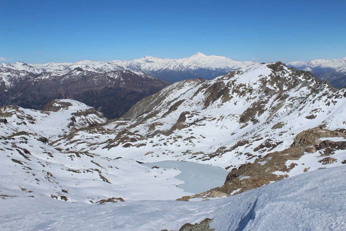 Cordillera de los Andes nevada con lago de montaña en primer plano