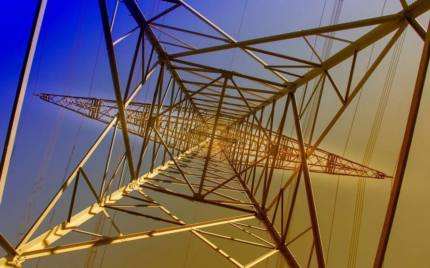 Estructura de una torre de transmisión de electricidad captada desde su base, con un cielo degradado de azul a dorado.