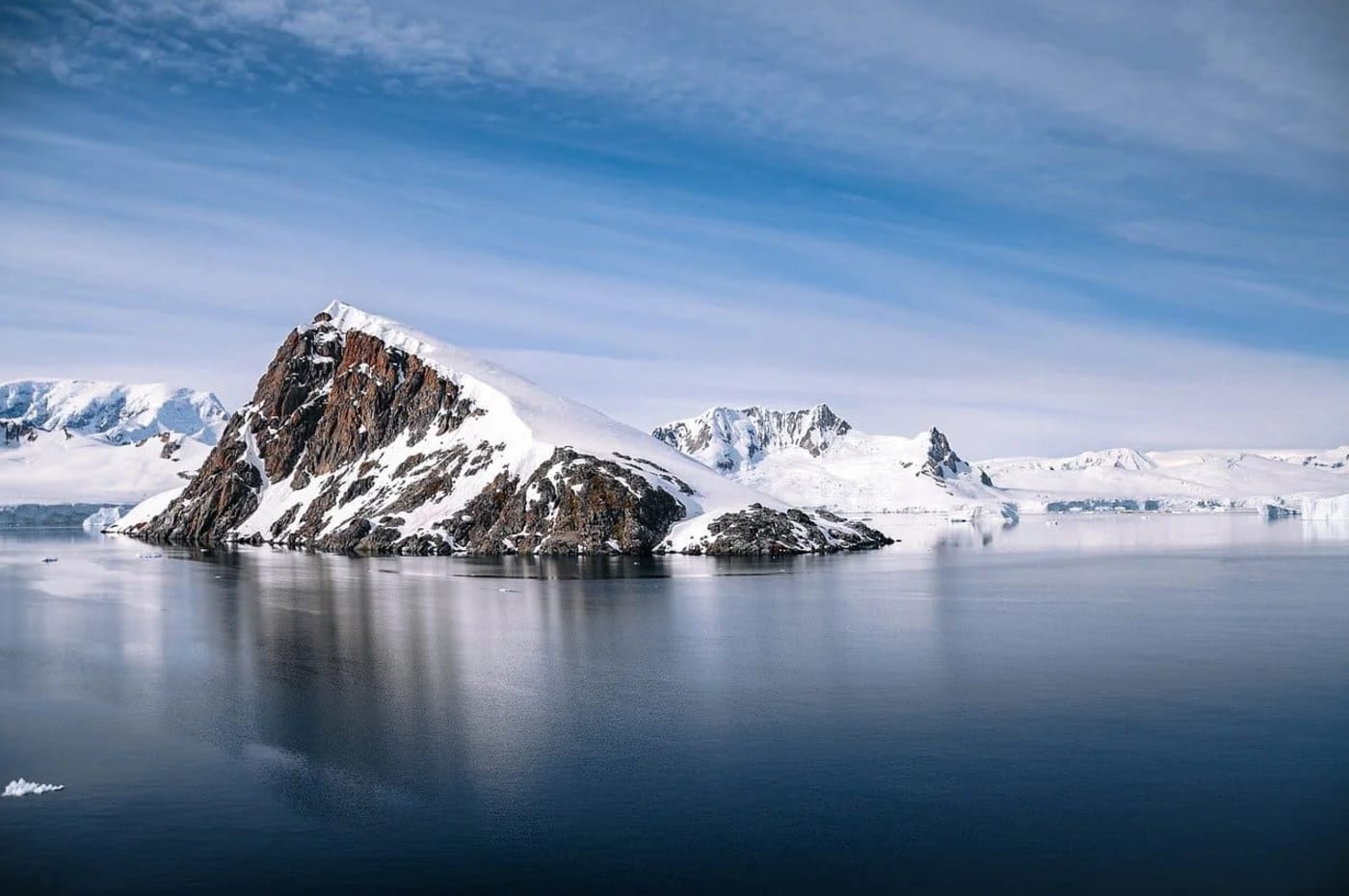 Isla rocosa cubierta de nieve rodeada de un océano tranquilo y cielo despejado en la Antártida.