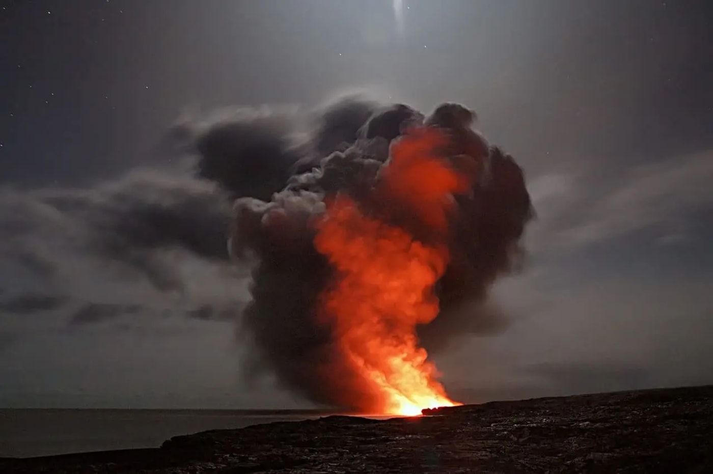 Erupción volcánica con una intensa nube de ceniza y lava iluminando el cielo nocturno.