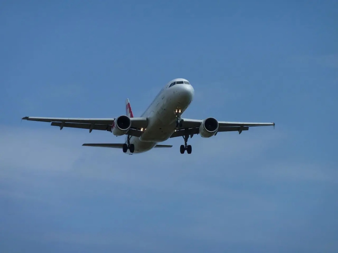 Avión comercial en aproximación para el aterrizaje, con sus trenes de aterrizaje desplegados y las luces encendidas, volando bajo un cielo despejado.