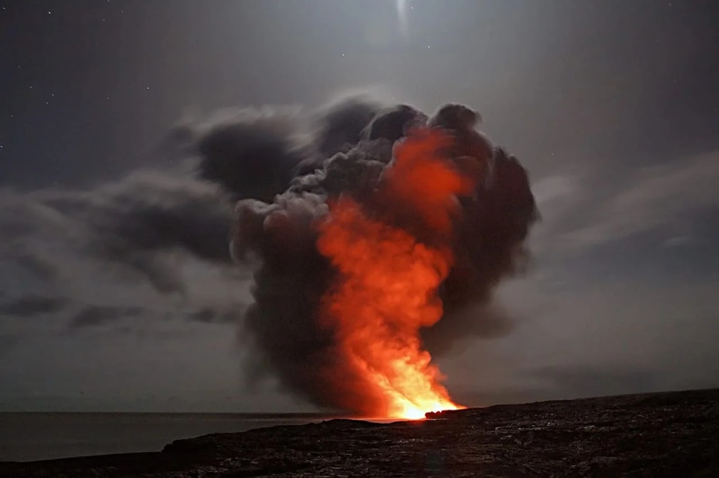 Erupción volcánica nocturna con una densa columna de humo oscuro y lava incandescente iluminando el cielo.