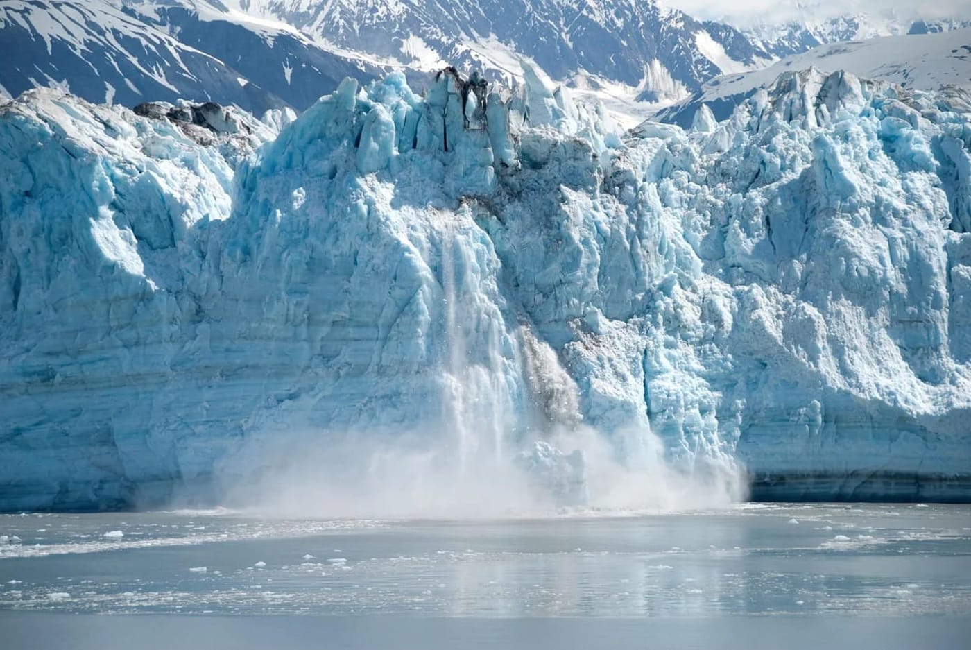 Un glaciar derritiéndose en un paisaje montañoso, con grandes fragmentos de hielo cayendo al agua en un proceso de deshielo visible.