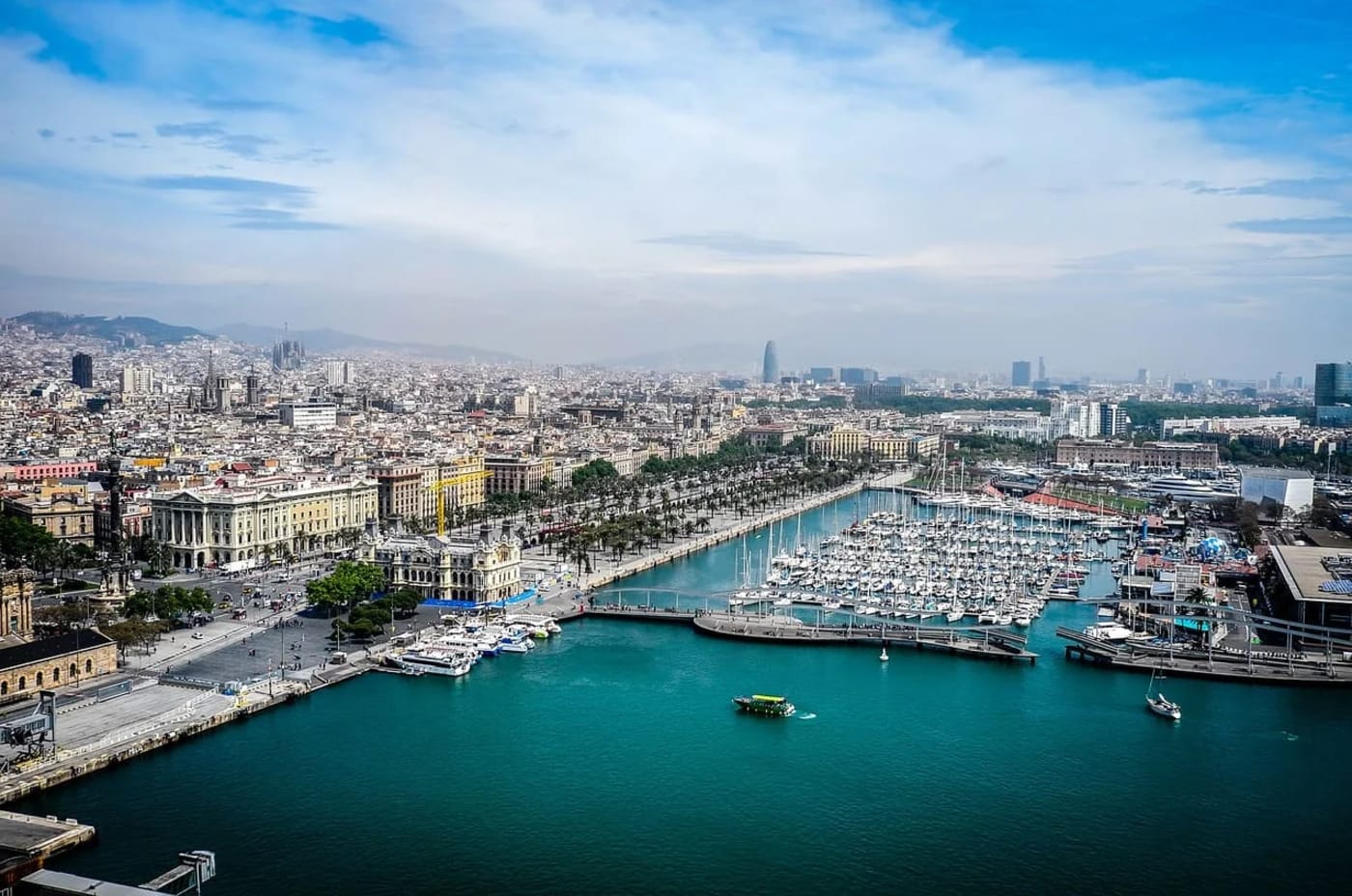 Vista panorámica del Puerto de Barcelona con numerosos barcos y edificios al fondo.
