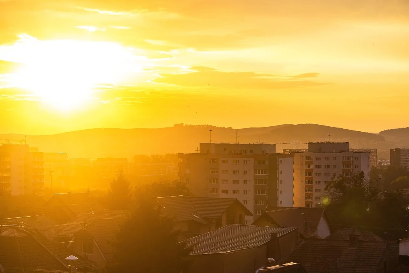 Atardecer con un sol intenso sobre una ciudad rodeada de montañas, generando una atmósfera cálida y dorada.