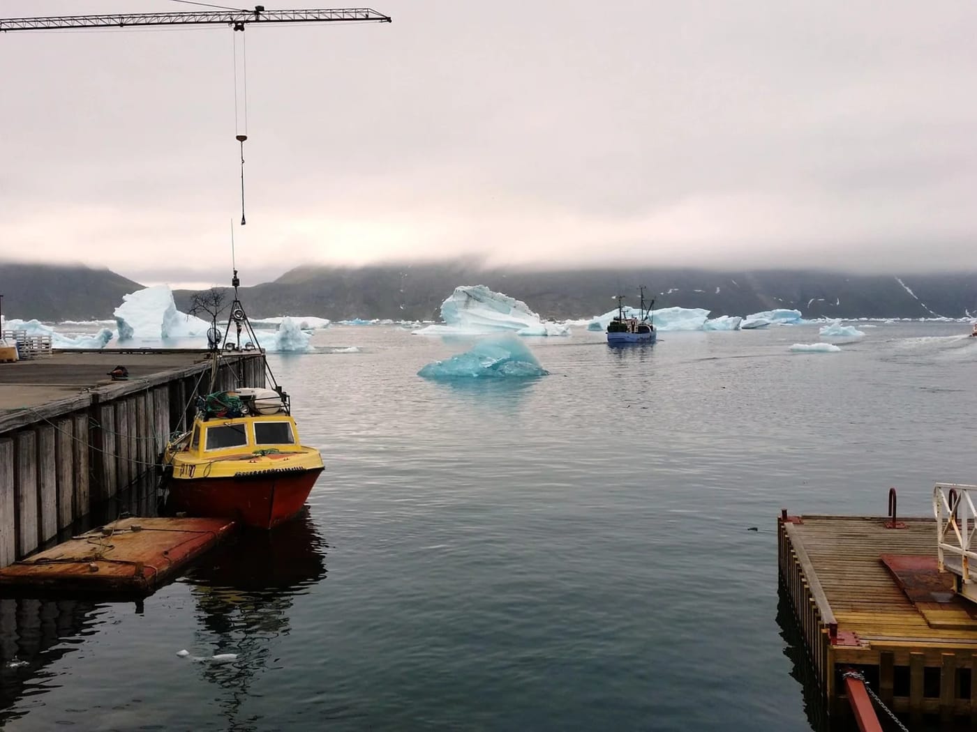 Botes en un muelle de Groenlandia con icebergs flotando en el fiordo