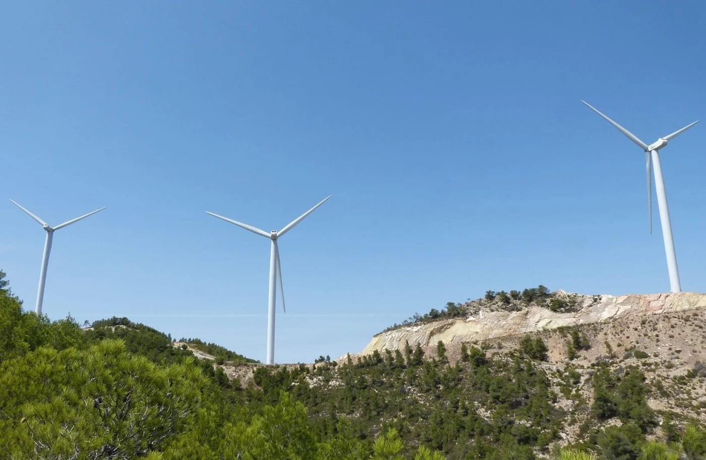 Turbinas eólicas sobre colinas cubiertas de vegetación, girando bajo un cielo azul despejado en un parque eólico