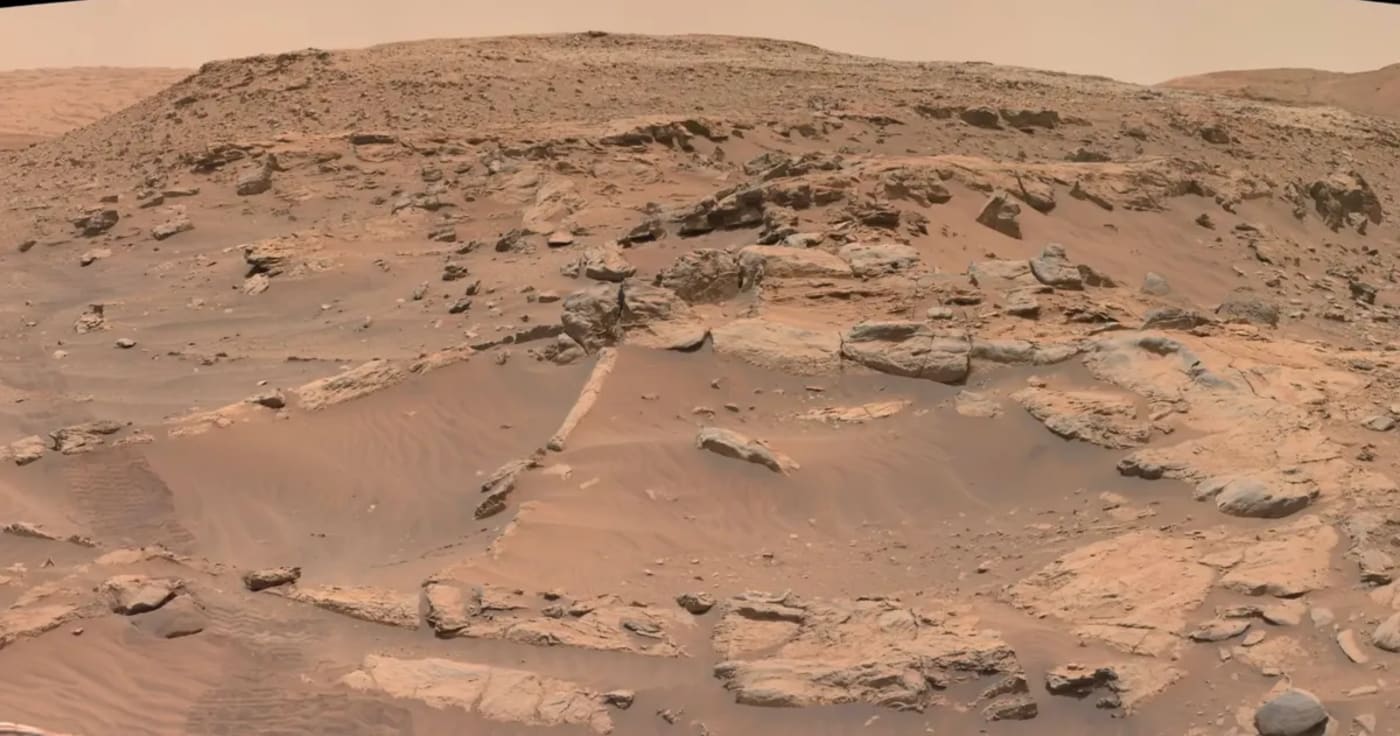 Panorama marciano captado por el vehículo explorador Curiosity, mostrando un terreno rocoso y arenoso en tonos rojizos