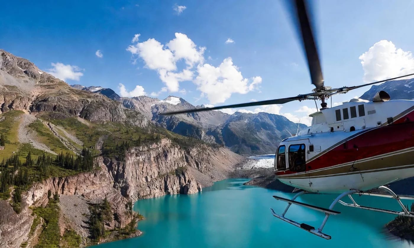 Un helicóptero sobrevuela un lago de agua turquesa rodeado de montañas en una zona remota de Alaska