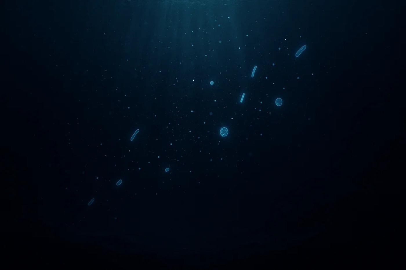 Oscuro océano profundo con haces de luz débiles, partículas brillantes y microbios luminosos flotando sobre un fondo abisal difuso