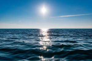 Superficie del océano iluminada por el sol bajo cielo despejado.