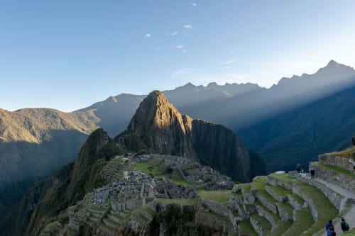 Vista panorámica de Machu Picchu al amanecer, iluminado por la luz solar y rodeado por montañas de la cordillera de los Andes.