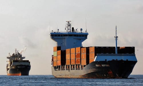 Un buque portacontenedores en el mar, cargado con decenas de contenedores apilados, y al fondo se distingue otro barco similar